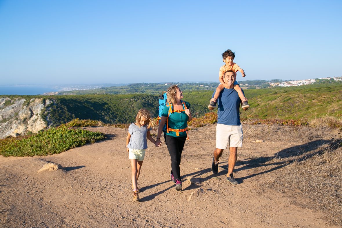 Happy family couple children hiking countryside walking path excited boy riding dads neck full length nature recreation concept